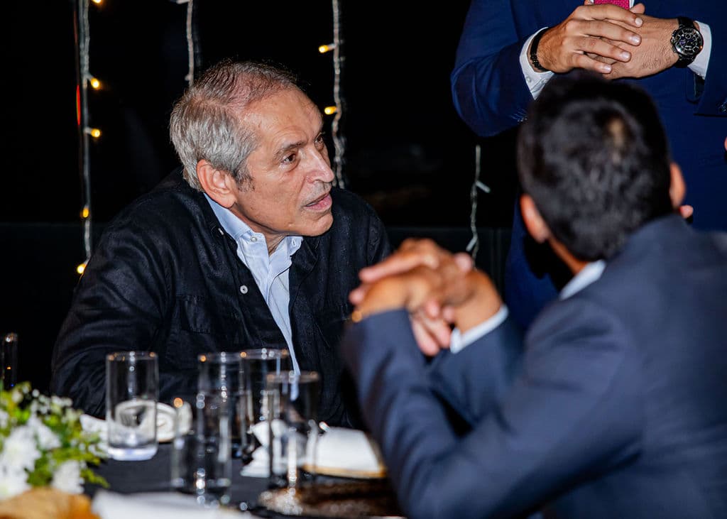 Guests in conversation at a candlelit gala dinner table strung with fairy lights