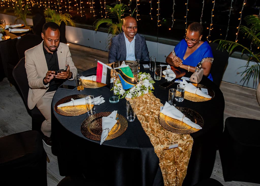 Guests smiling at a gold-themed gala dinner table set with Tanzania and Egypt flags