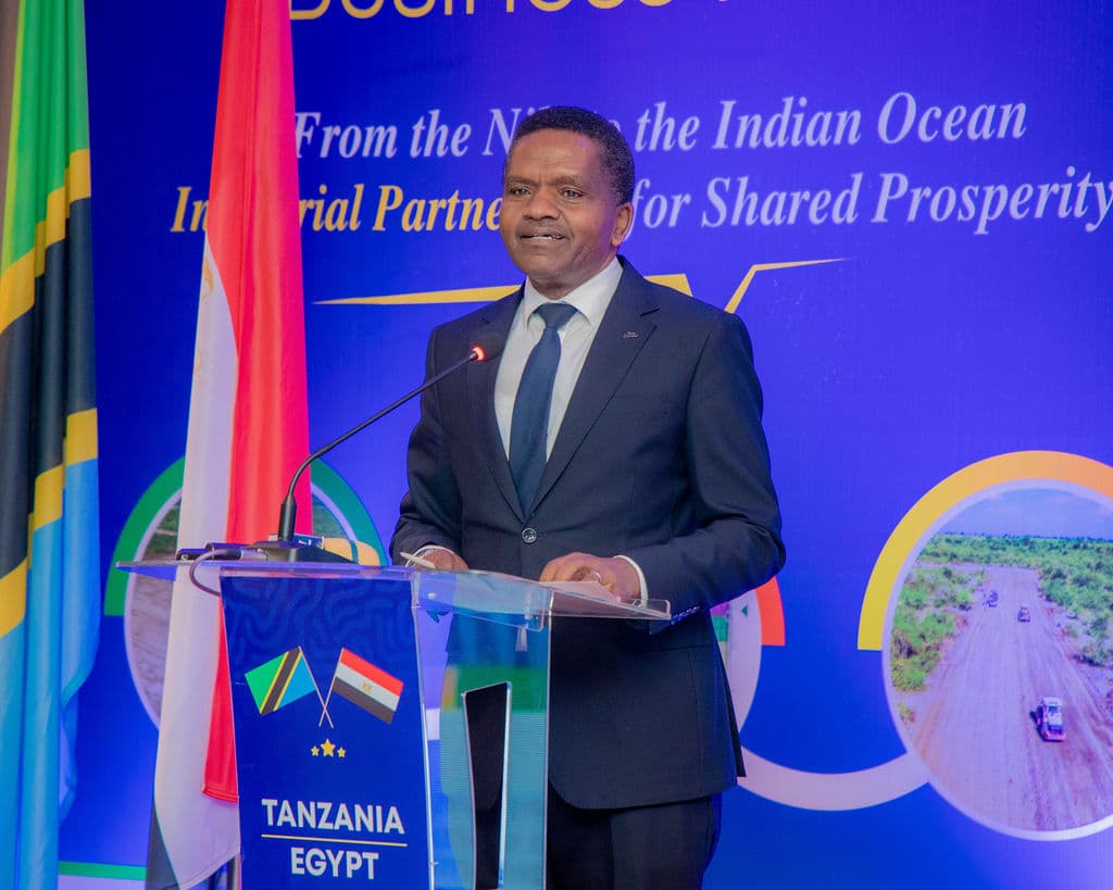Speaker addressing the forum from the podium in front of the branded LED screen